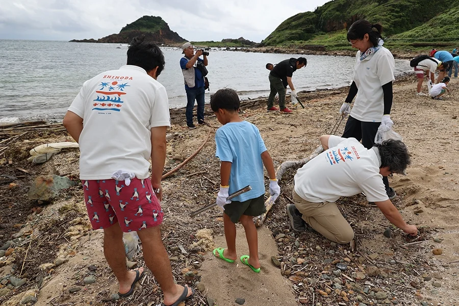海岸で大人と子供たちが協力してゴミを拾うビーチクリーン活動の様子