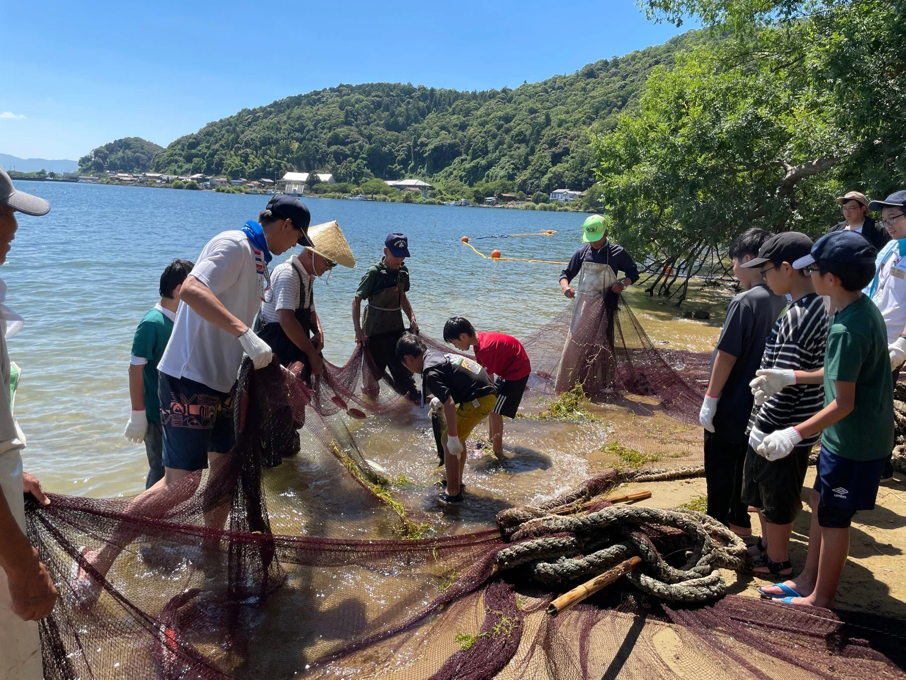 子供と大人が網で魚を捕っている画像