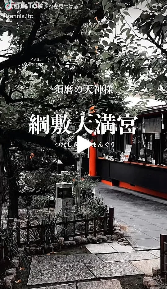 須磨にある綱敷天満宮の様子を捉えた画像です。緑豊かな木々に囲まれた境内には、黒と赤のアクセントが印象的な社殿が見え、石畳の道が続いています。静かで厳かな日本の風景が広がっています。
