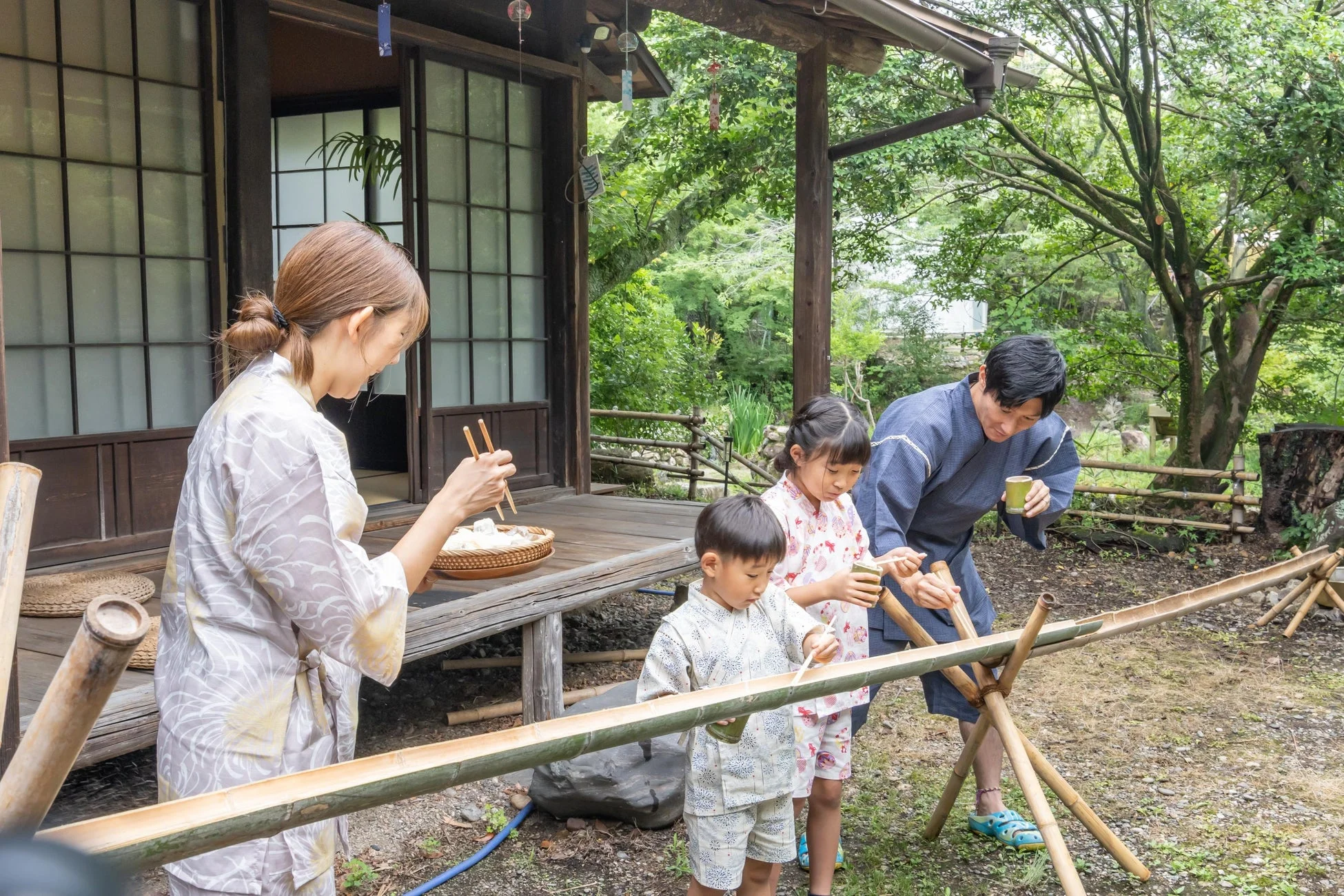 夏の日、浴衣姿の家族が日本家屋の庭で流しそうめんを楽しむ風景