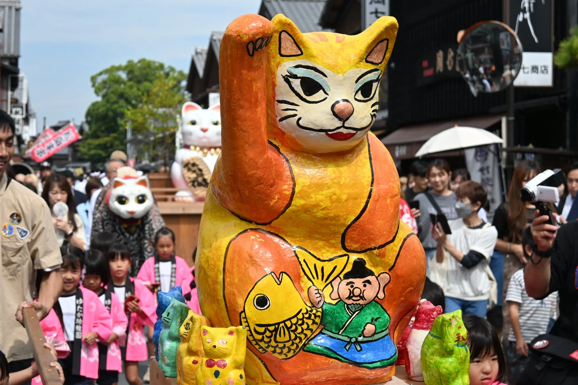 日本の祭りで、巨大なカラフルな招き猫が主役のパレードの様子