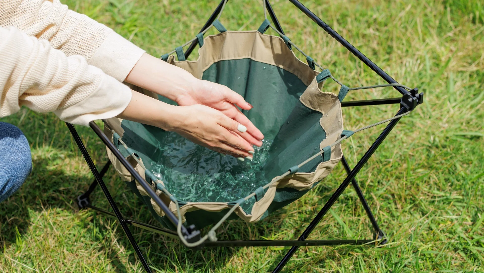 屋外で、女性が折りたたみ式の洗面器に入った水で手を洗っています。