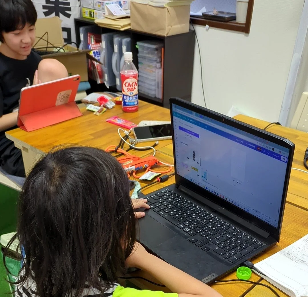 テーブルで二人の子供がそれぞれノートパソコンとタブレットを使用している様子。一人は真剣に画面を見つめ、もう一人は笑顔でタブレットを操作しており、学習や遊びに集中している日常の風景です。