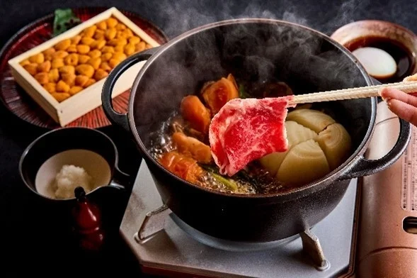 湯気が立つ鍋に霜降り牛肉を入れようとしている様子