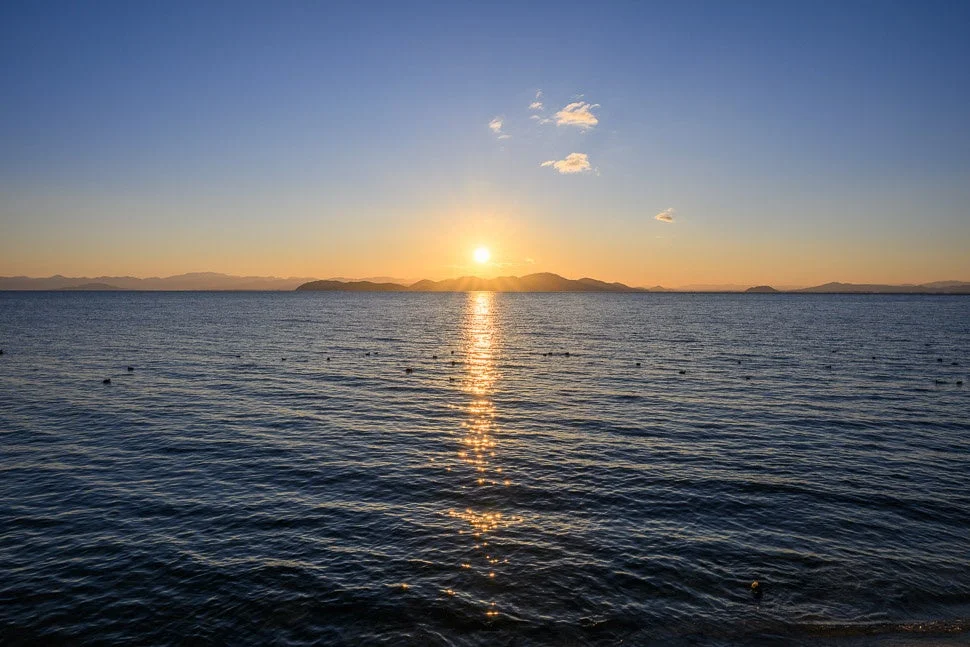 夕日が水面に反射し、遠くの山々がシルエットになった美しい海の風景
