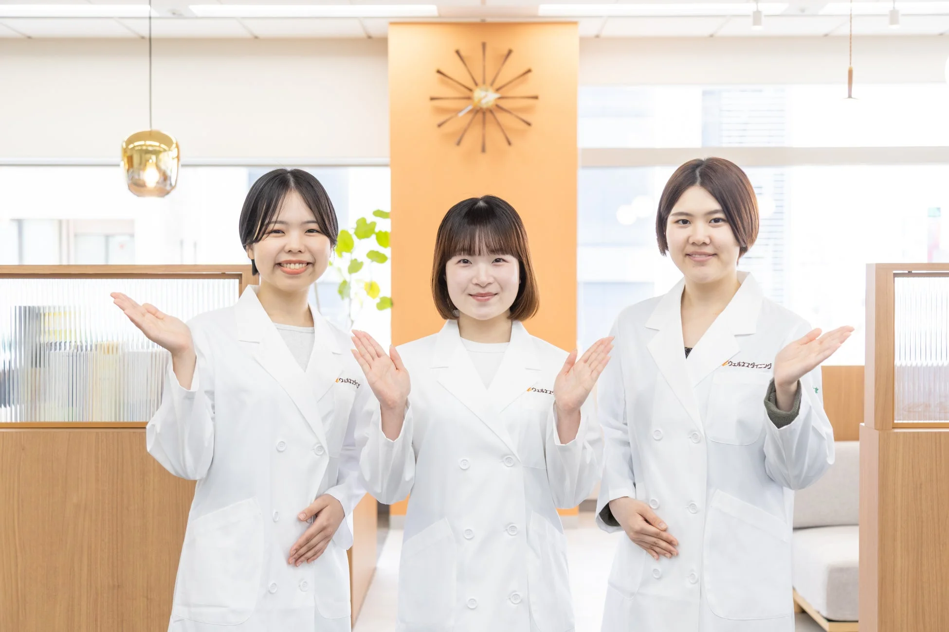 白衣を着た3人の女性が笑顔で両手を広げ、案内している様子