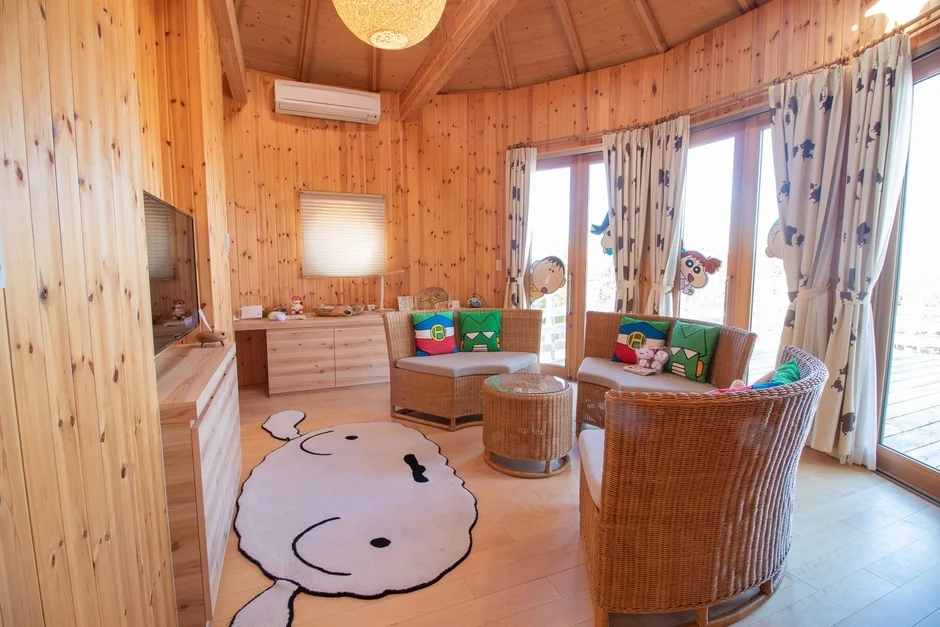 木製のリビングルームにクレヨンしんちゃんのキャラクターグッズが配置された客室