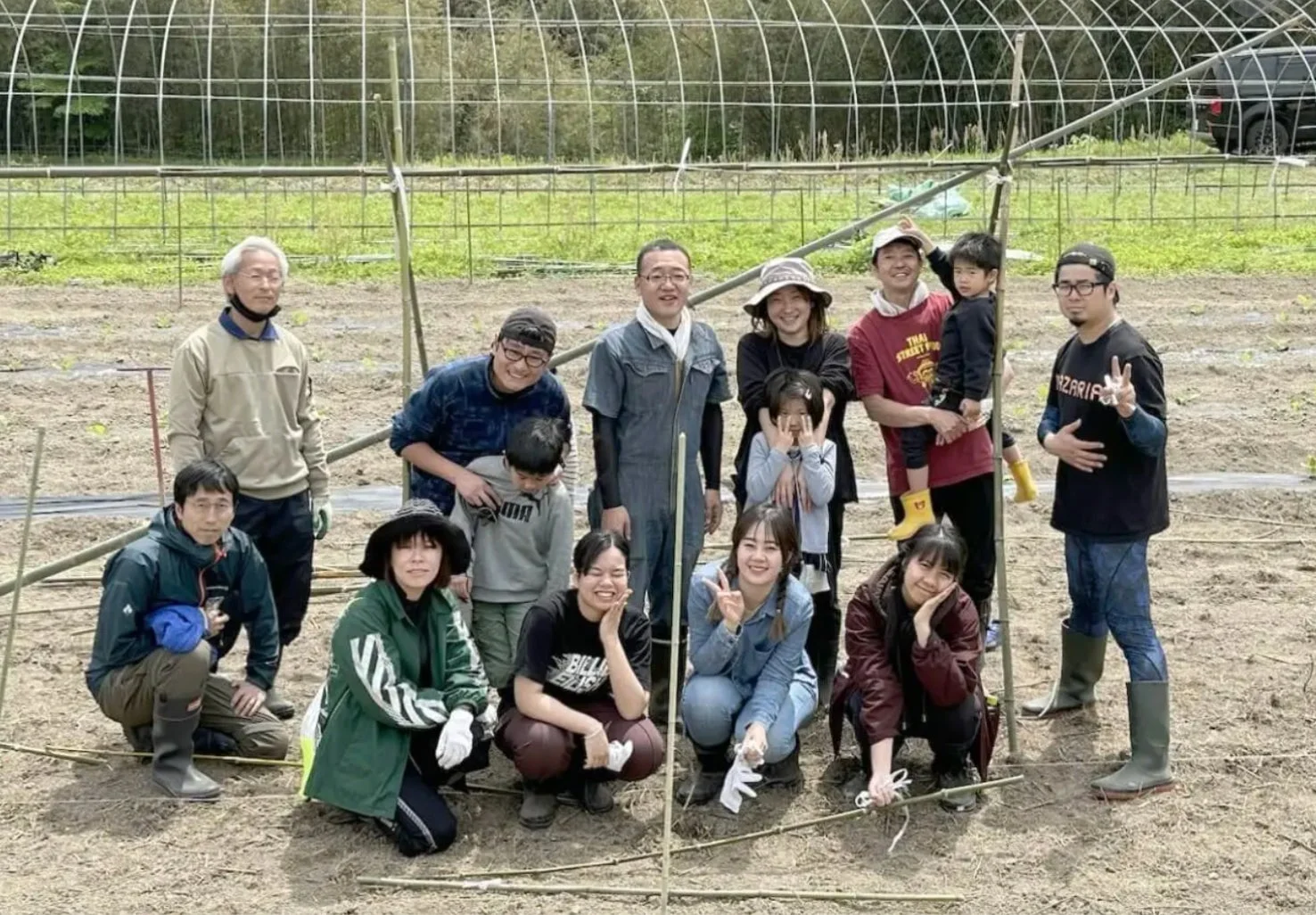 畑で多くの人々が集合写真を撮っています。子供から大人、高齢者まで様々な年代の男女が笑顔で写っており、共同で農作業を行っている様子がうかがえます。