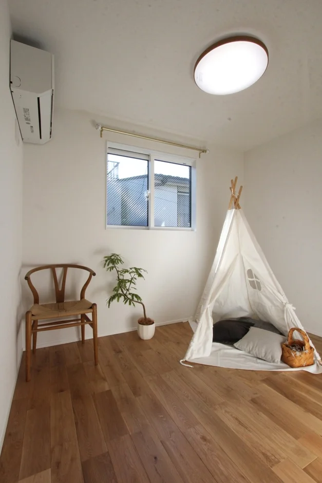 明るい木目のフローリングの部屋で、白を基調としたシンプルでナチュラルなインテリアが特徴です。ティピーテント、木製の椅子、観葉植物が配置され、子供部屋やリラックススペースに最適です。