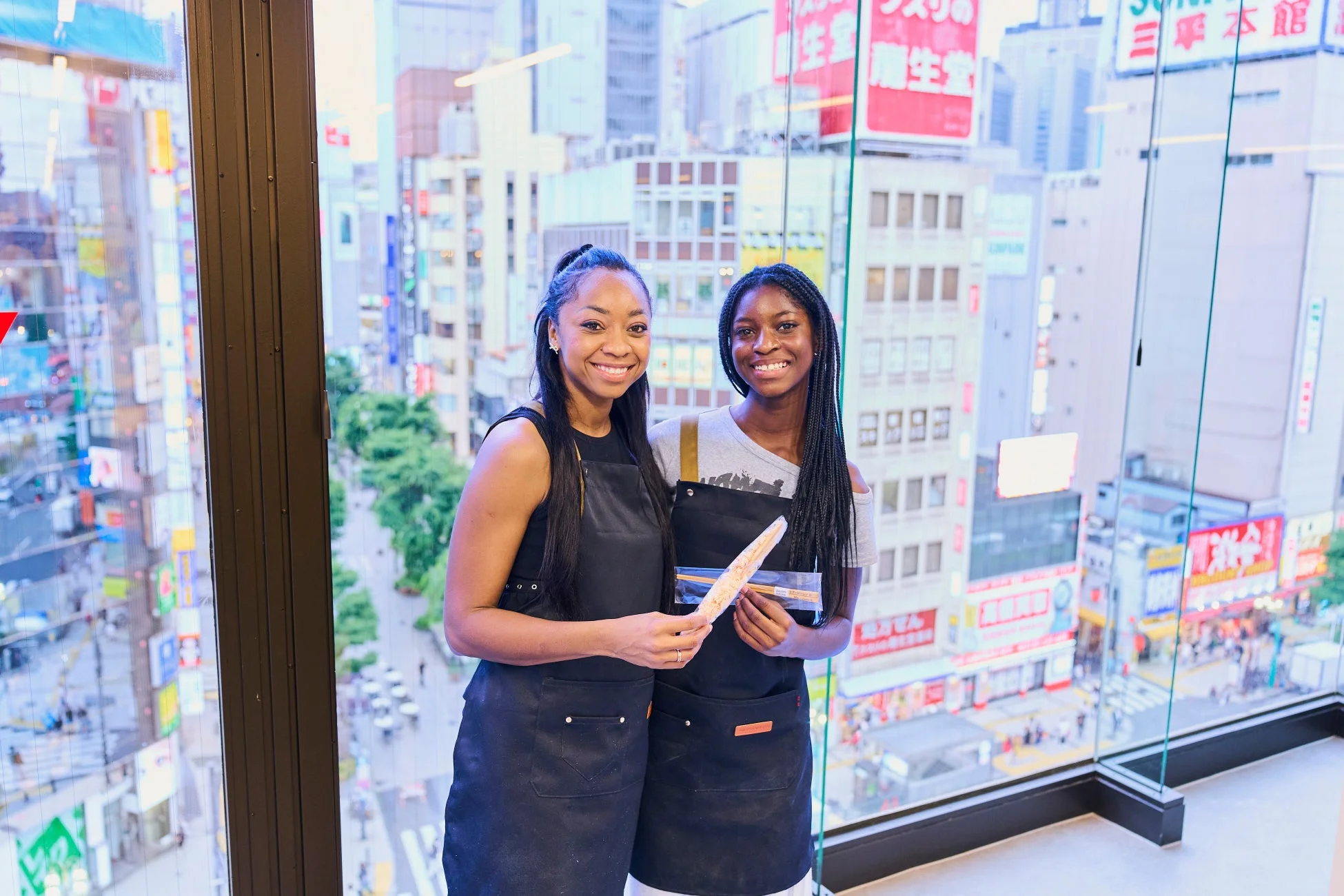 女性二人が箸を持って笑顔、都市風景