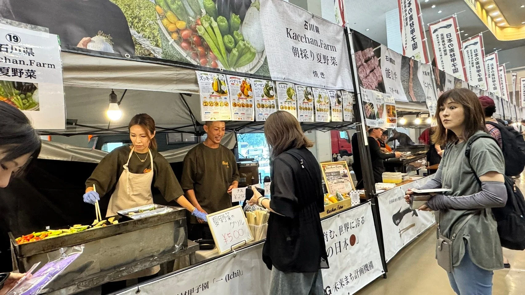 屋内のイベント会場で、石川県の「Kacchan.Farm」が朝採り夏野菜のグリルを販売している様子