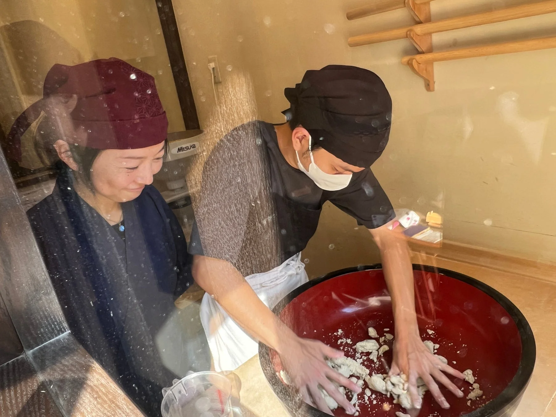 職人が大きな赤いボウルで生地を捏ねている様子を、女性が見守っています。