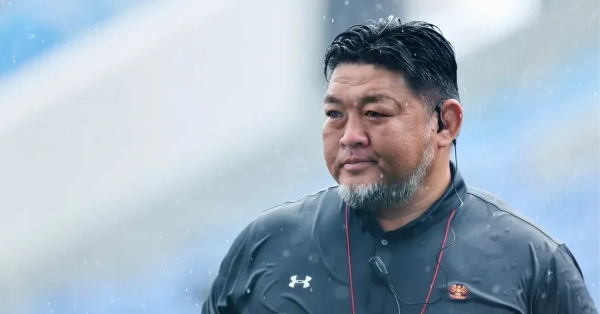 雨が降る屋外で、黒いスポーツウェアを着た中年男性が写っています。