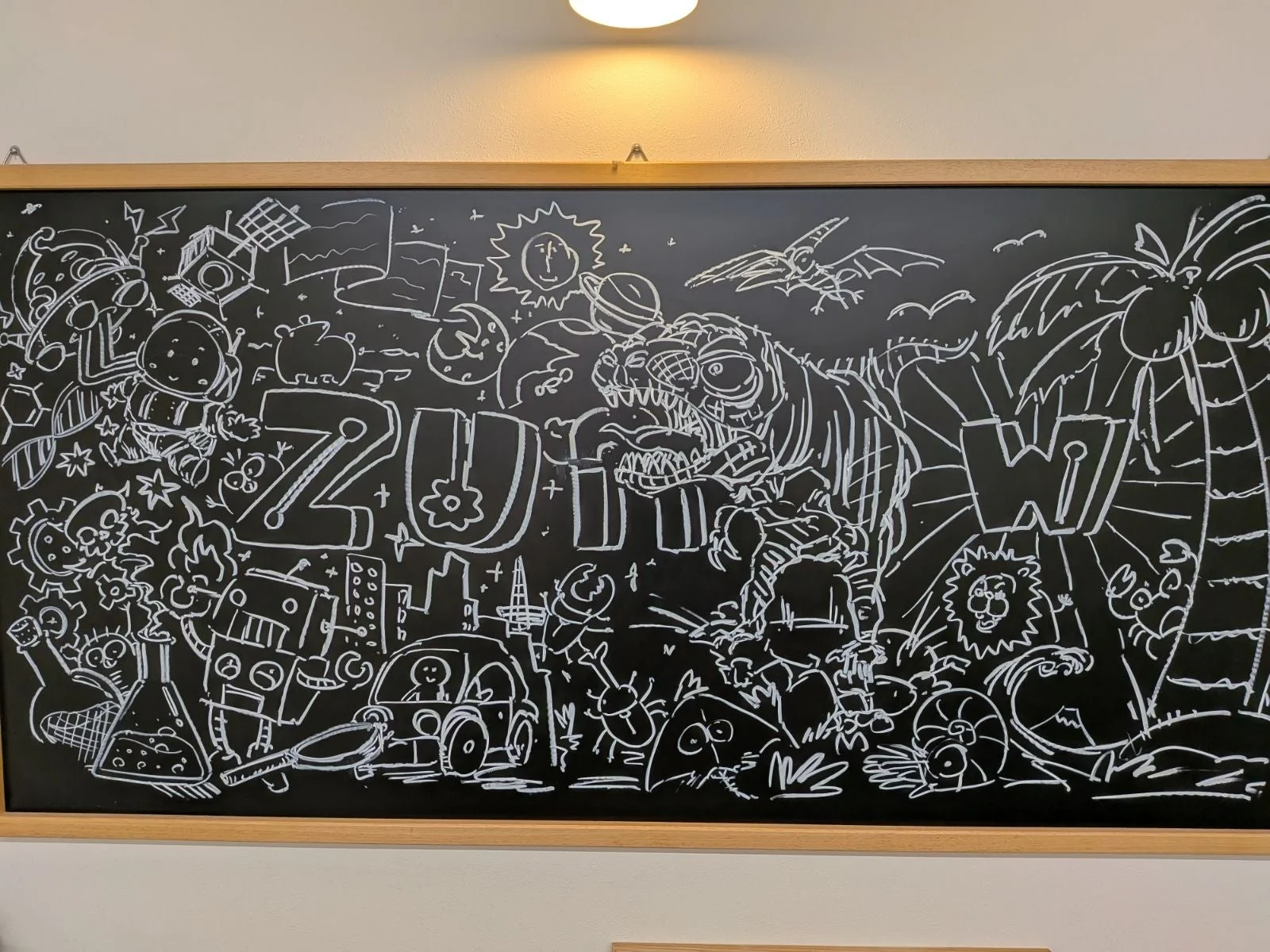 黒板に白チョークで描かれた、宇宙、恐竜、ロボット、都市、自然など多様な要素が混在する詳細なアート作品。