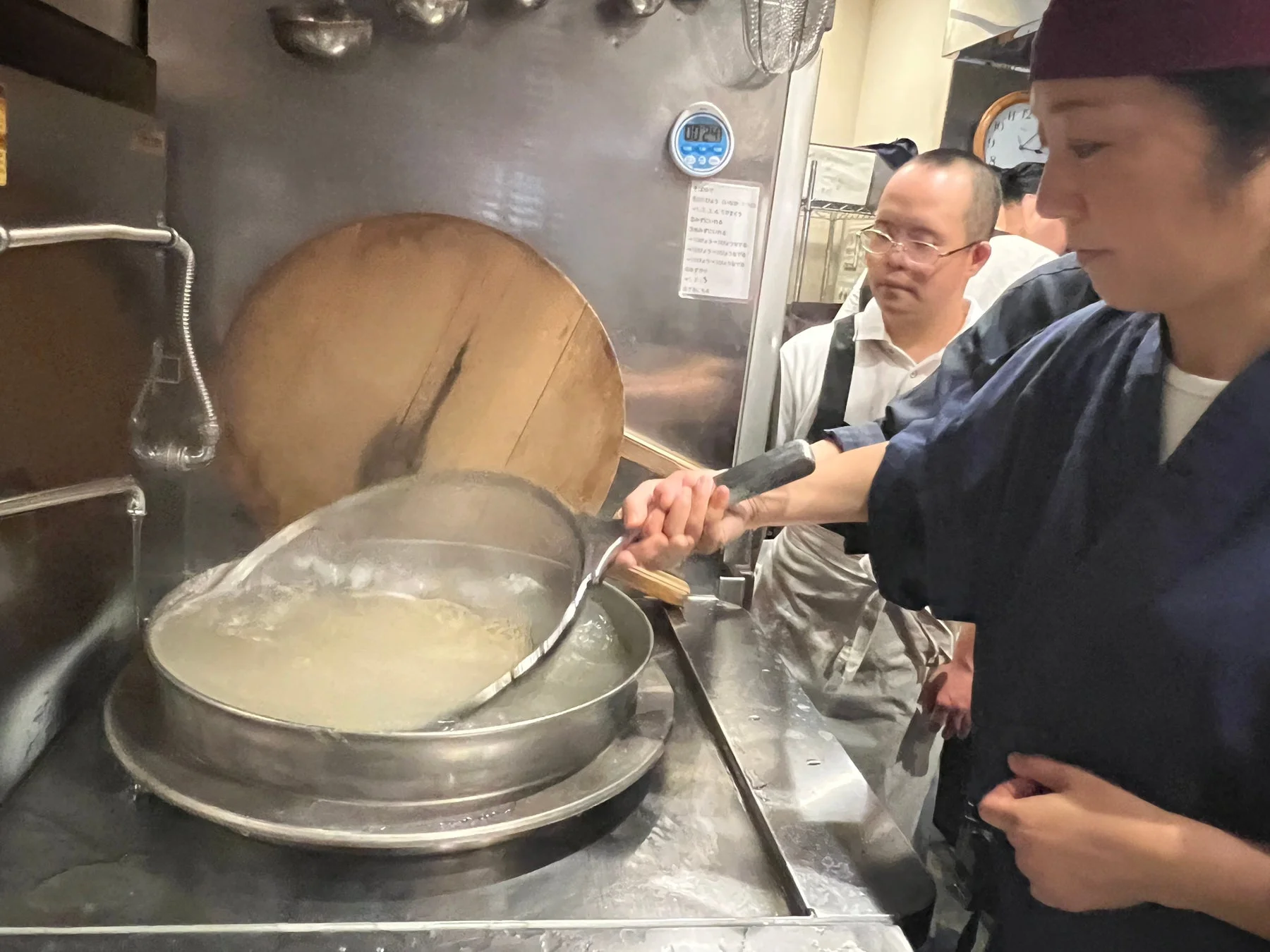厨房で調理師が大きなざるを使って麺を茹でている様子。