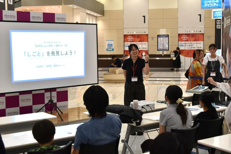 ショッピングモール内で開催されている名城大学主催のキッズサマースクール。女性講師が「しごと」を発見しようというテーマでプレゼンしており、子どもたちが熱心に聞き入っている様子
