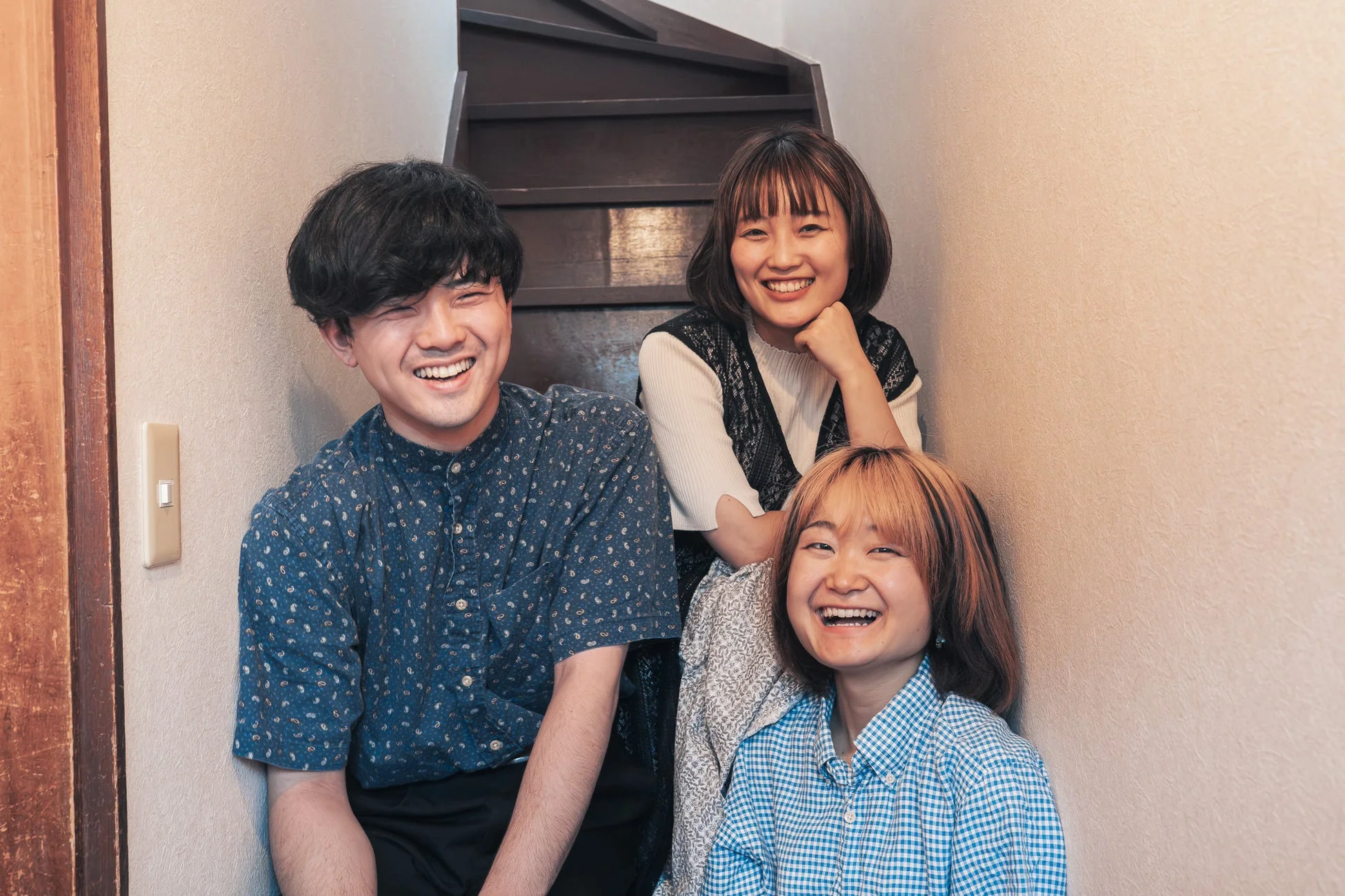 室内で階段のそばで楽しそうに笑う3人の若者