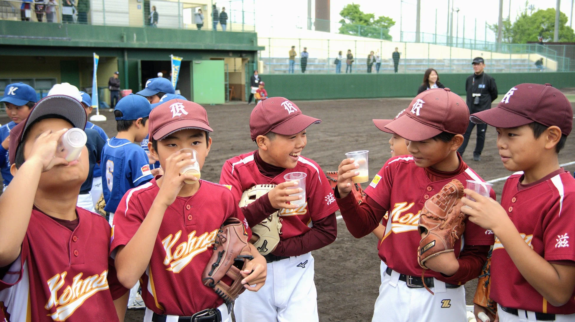 野球のユニフォームを着た少年たちが、グラウンドで休憩中に飲み物を飲んでいる様子