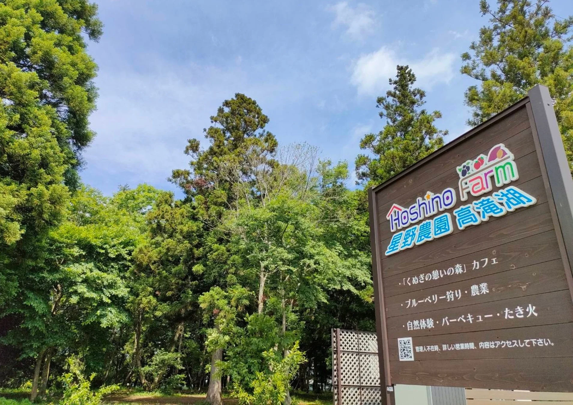 青空と緑豊かな森を背景に「星野農園 高滝湖」の看板が立っています。看板にはカフェ、ブルーベリー狩り、自然体験、バーベキューなどの施設やアクティビティが案内されており、アウトドアレジャーを楽しめる場所であることがわかります。