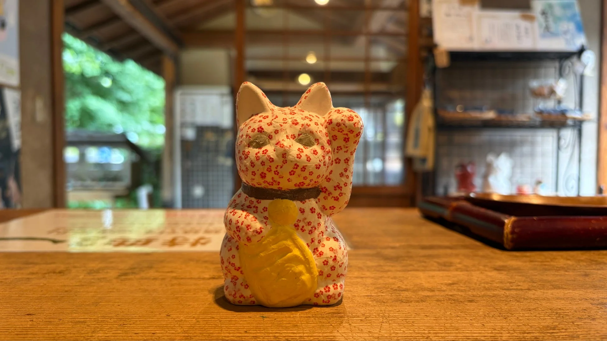 木製のテーブルに、赤と白の花柄模様が施された招き猫の置物が飾られています