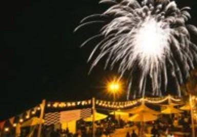 夜空に咲く大輪の花火と、その下で賑わう屋外イベント会場