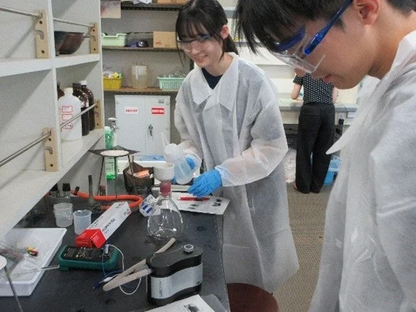 白衣と安全眼鏡を着用した学生が化学実験を行う様子