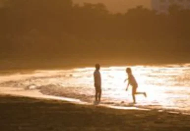 夕焼けの海辺で、2人の人物がシルエットになって立っている