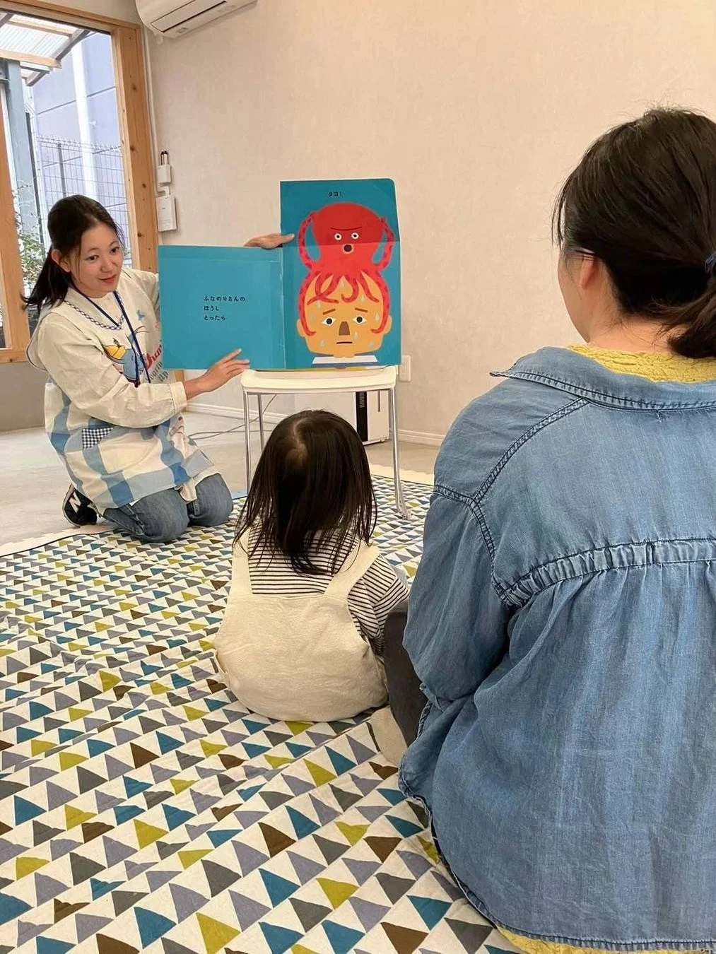 保育士が子供と保護者に絵本の読み聞かせをしている場面