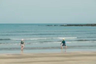青い空と広がる海を背景に、2人の人物が砂浜の水際を歩いている