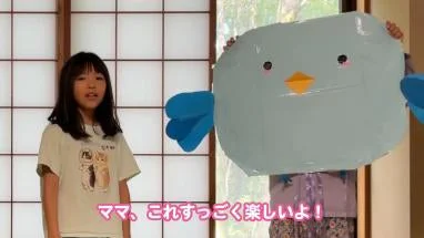 室内で水色の鳥のキャラクターの隣に立つ女の子