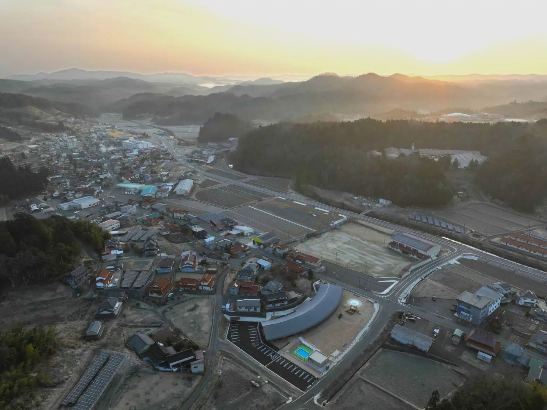 早朝、山々に囲まれた日本の田舎町の空撮です。