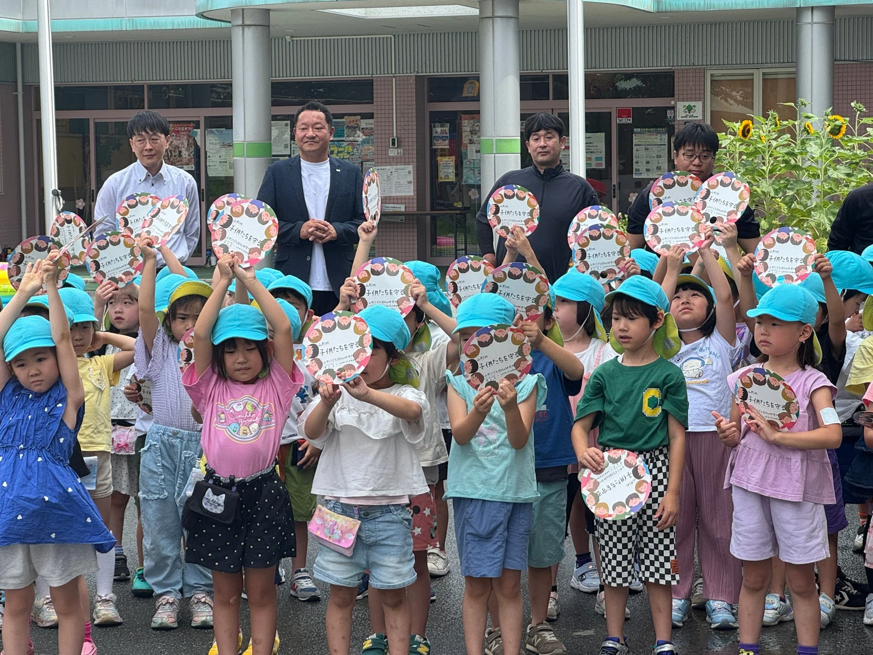 子どもたちとSDGsのメッセージが書かれたうちわを掲げる人々の様子