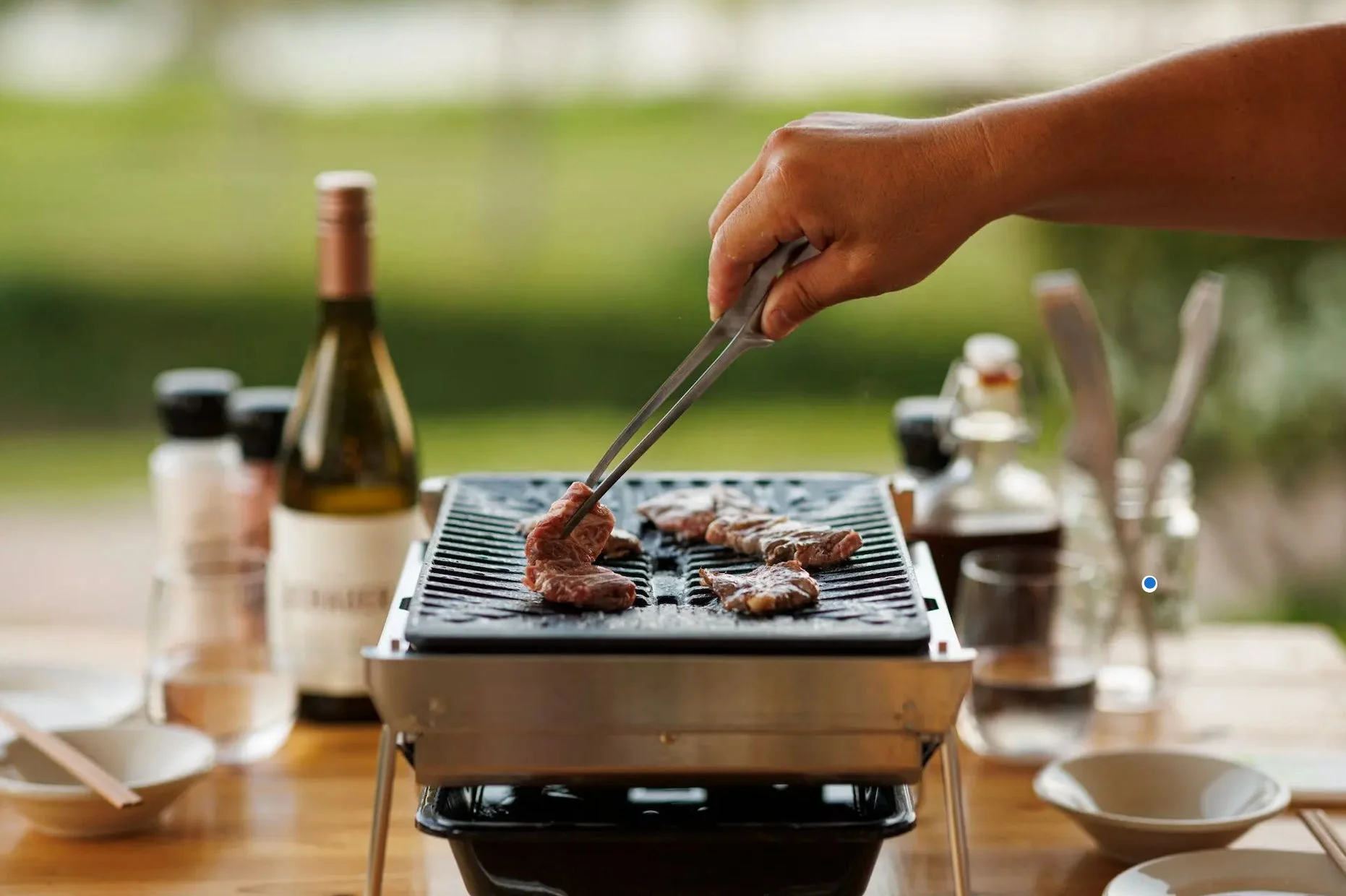 屋外でポータブルグリルを使って肉を焼いている様子