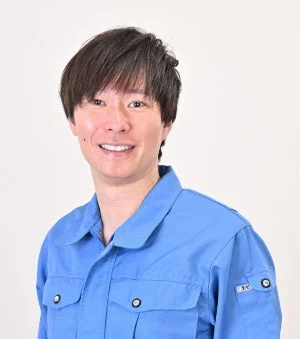 青い作業着を着て笑顔を見せる男性