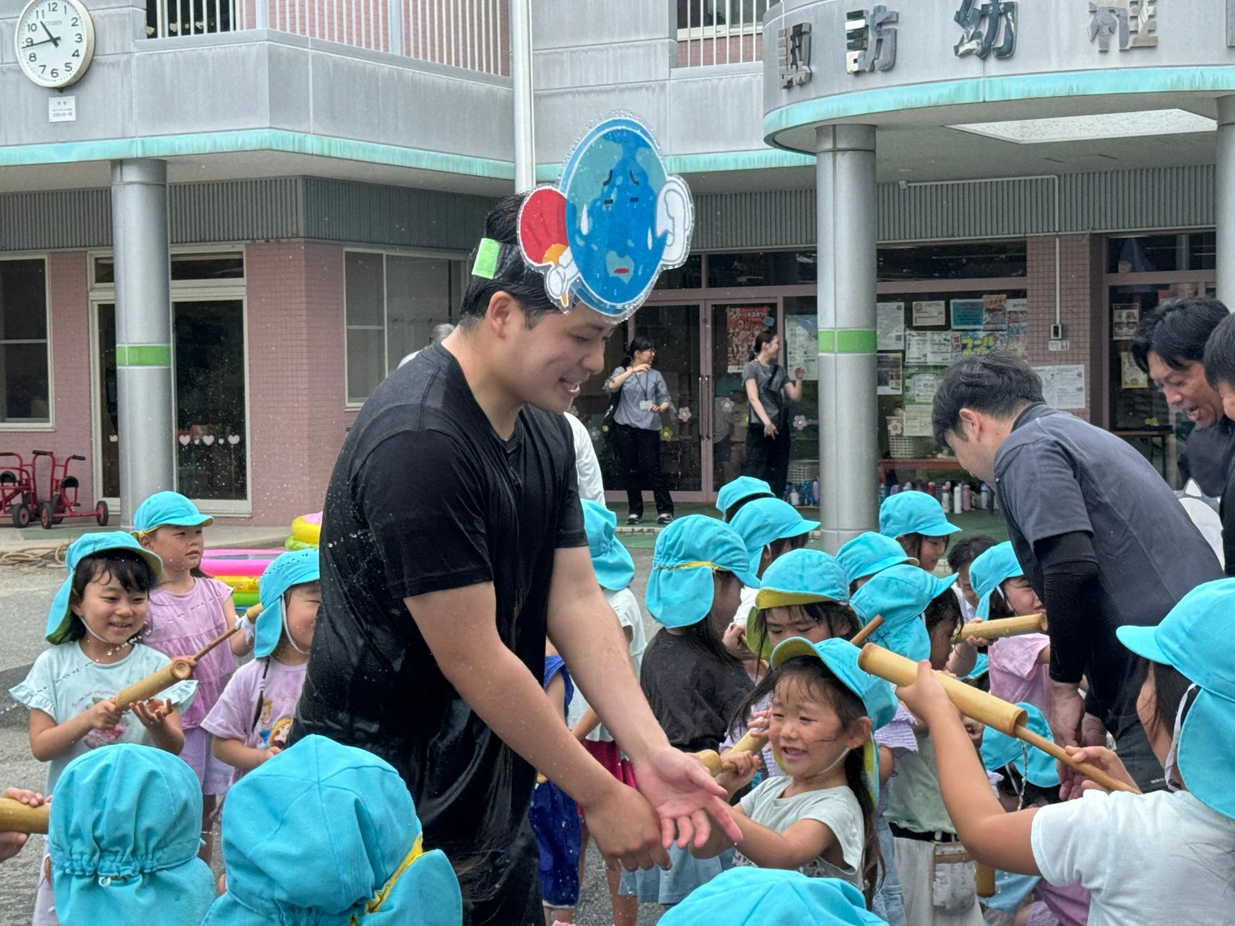 幼稚園で水遊びを楽しむ子どもたちと地球の着ぐるみを着た男性