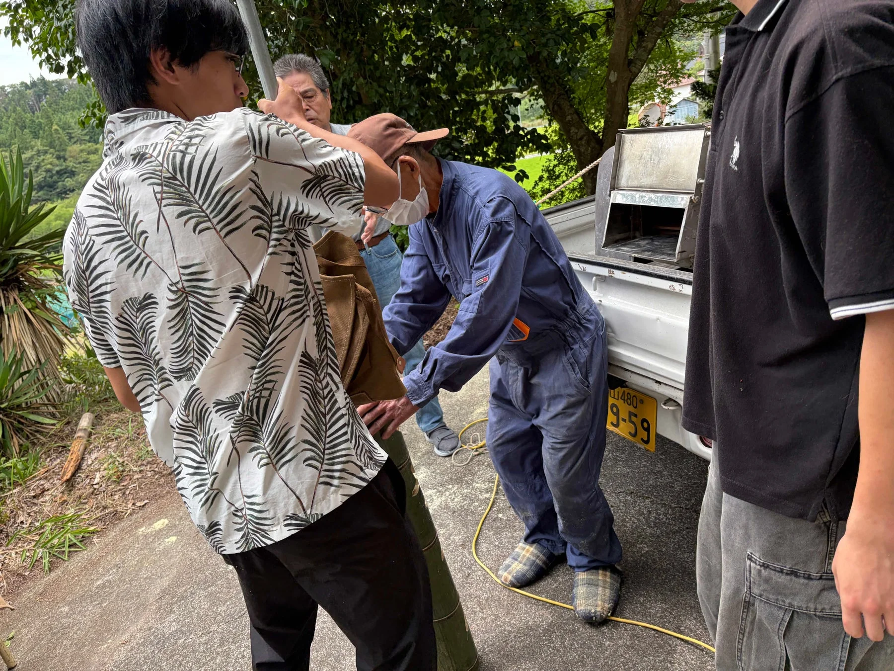 屋外で数人の男性が白い軽トラックの周りで作業をしている様子
