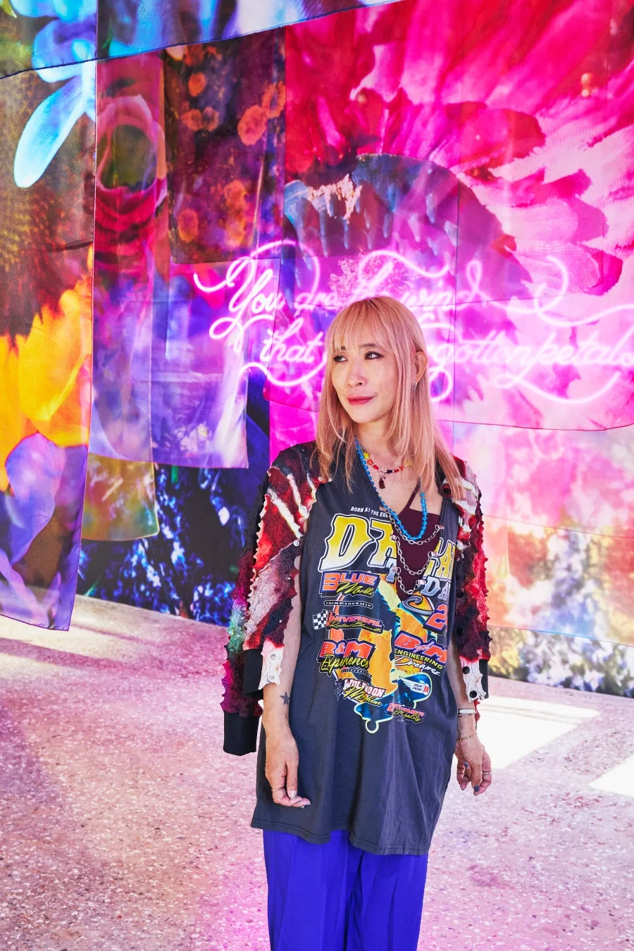 ピンクの髪の女性が鮮やかなアートインスタレーションを背景に立つポートレート