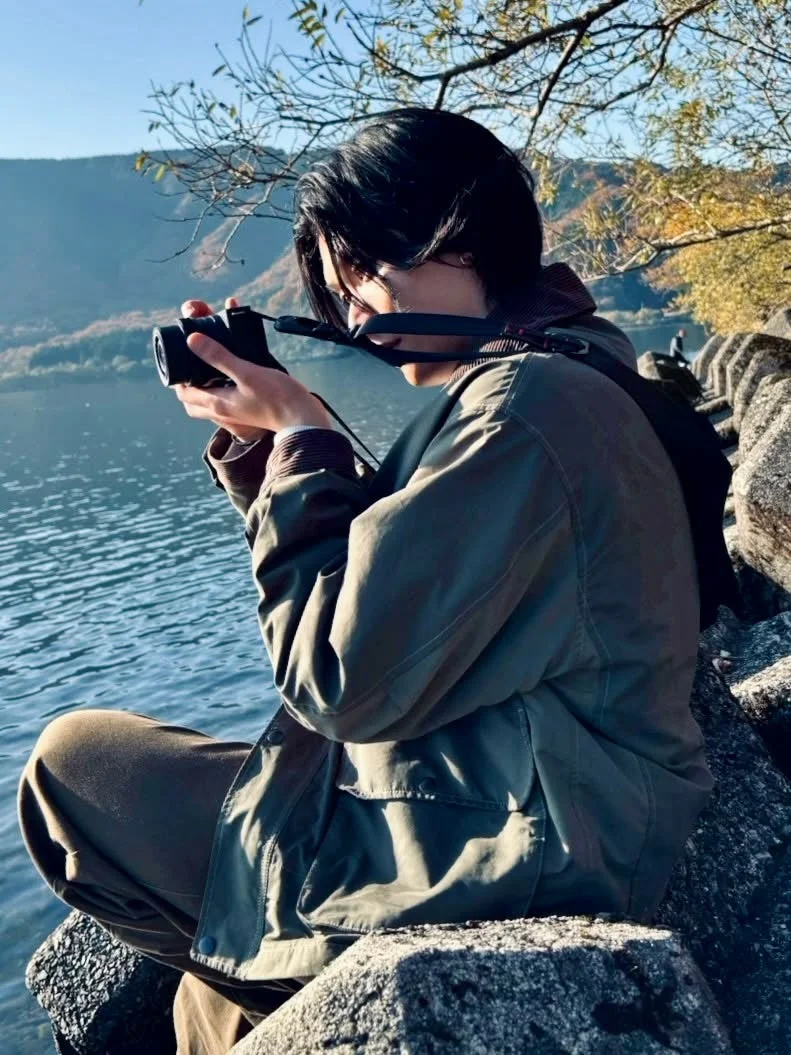 湖畔の岩に座り、カメラで美しい風景を撮影している男性の姿