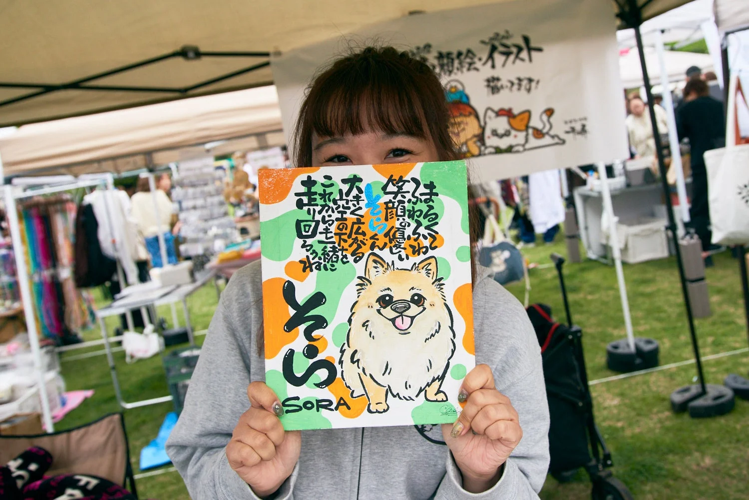 犬のイラストと「そら」という文字が描かれた絵を掲げる女性