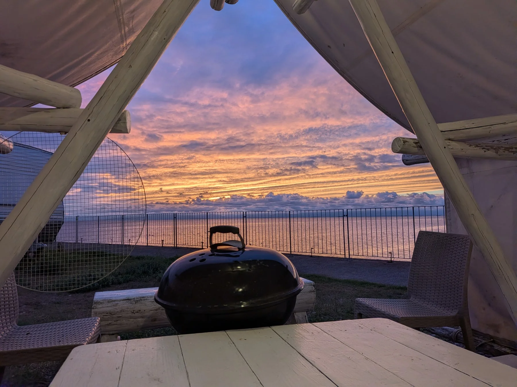 夕焼け空と海を望むテントの中からバーベキューグリルを捉えた画像