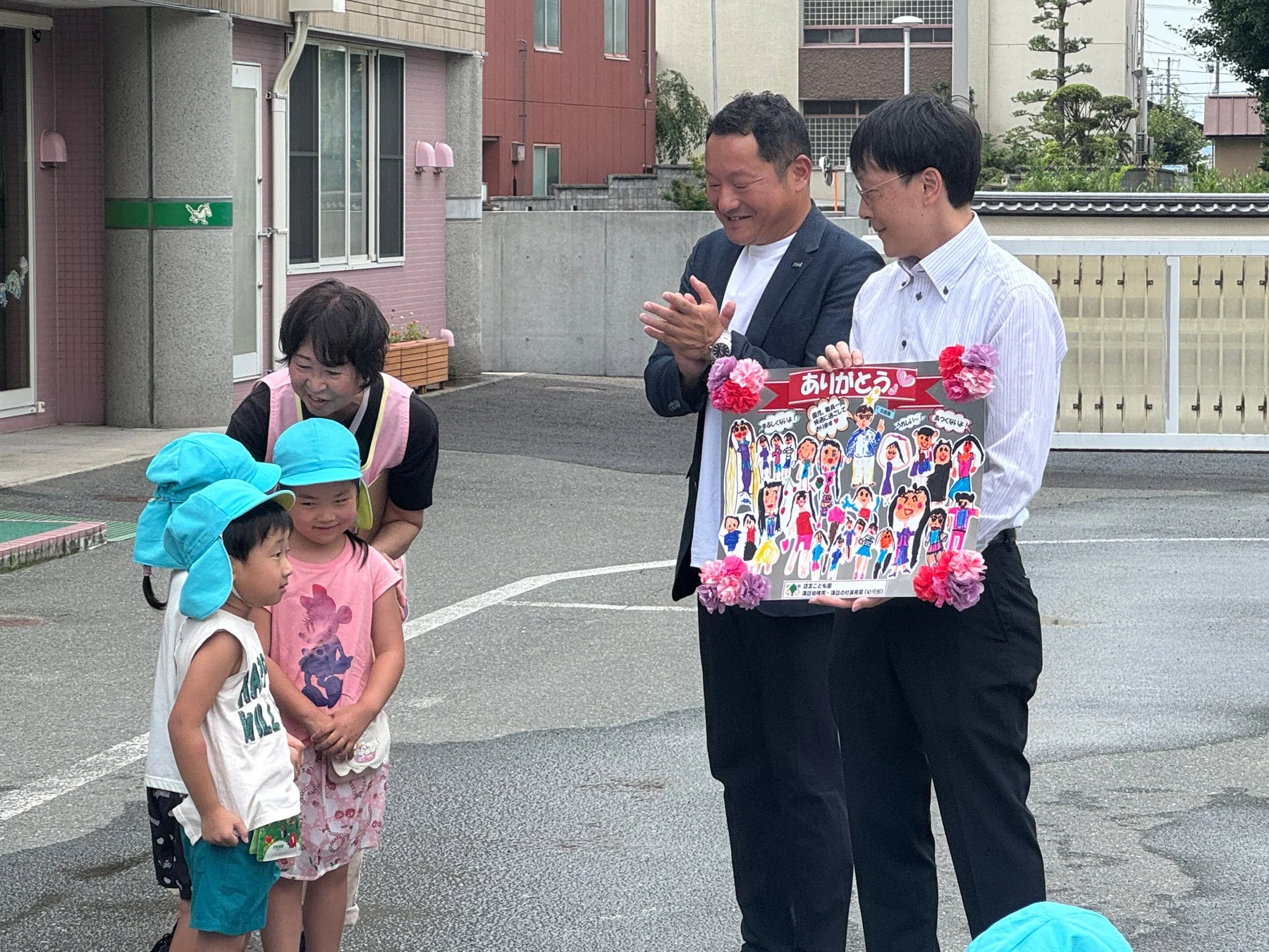 園児と先生が男性二人に感謝ボードを贈呈している様子