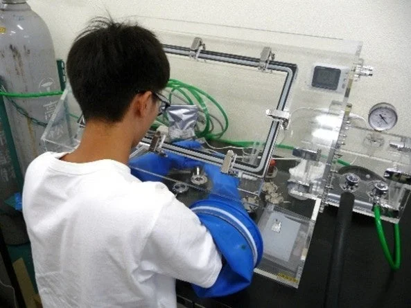 グローブボックス内で実験作業を行う人物