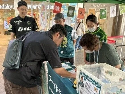 屋外のイベントブースでフードドネーションの箱を前に集まる人々